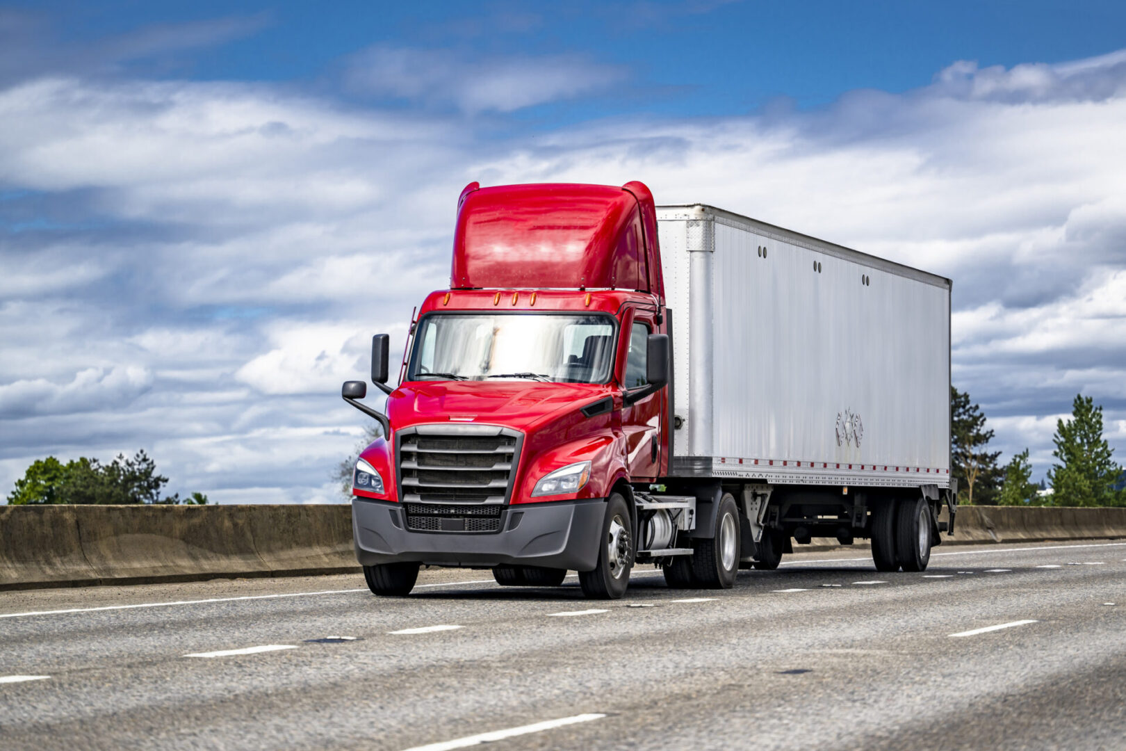 Red semi-truck driving on open highway.